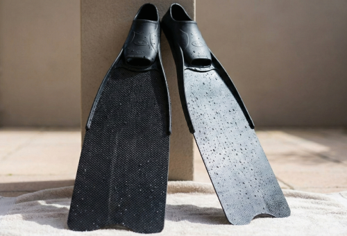 The fins are propped against a wall on a towel to air dry in a shaded location, protecting them from harmful sunlight.